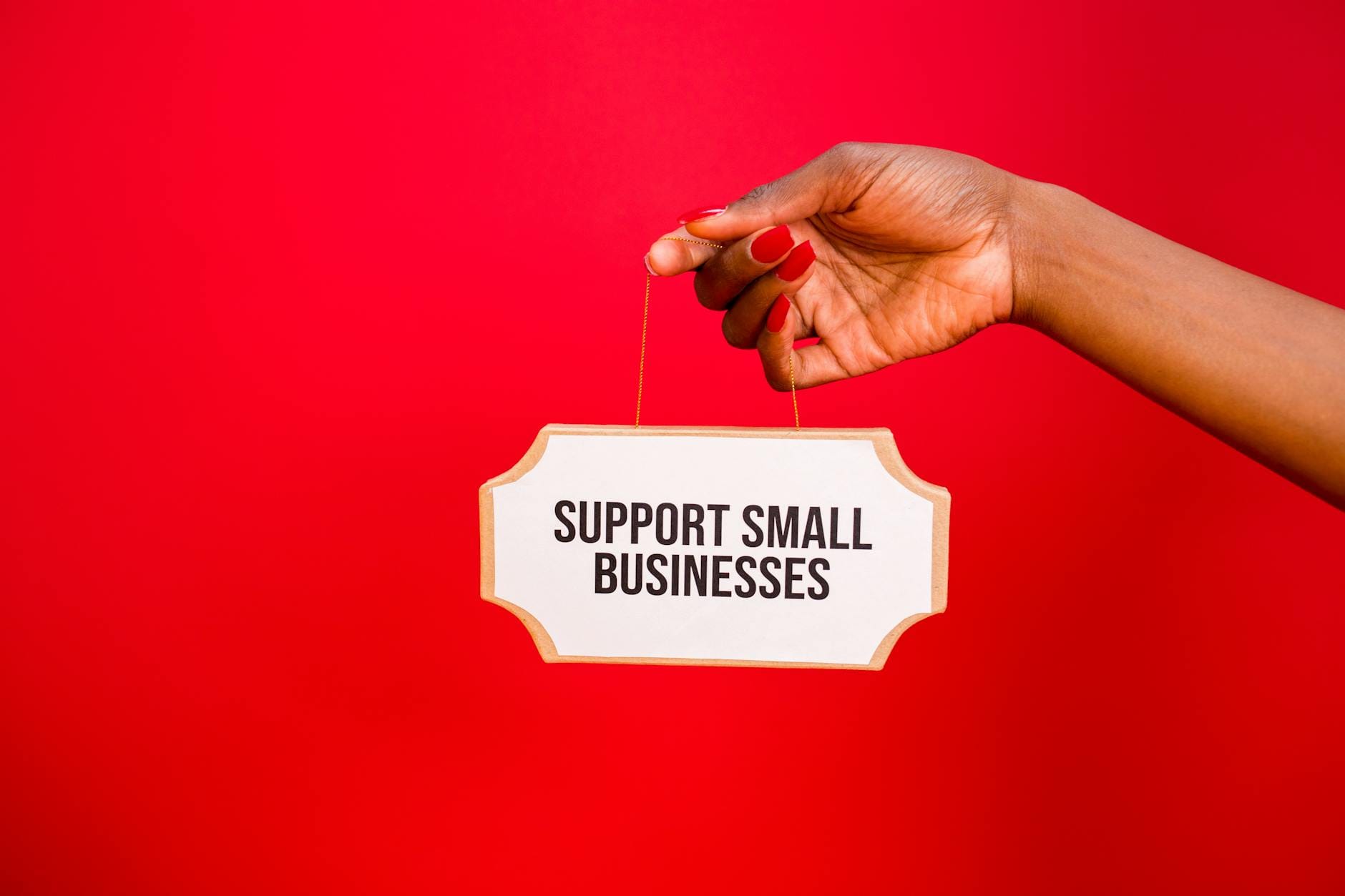 Dłoń trzymająca tabliczkę Support Small Businesses na czerwonym tle