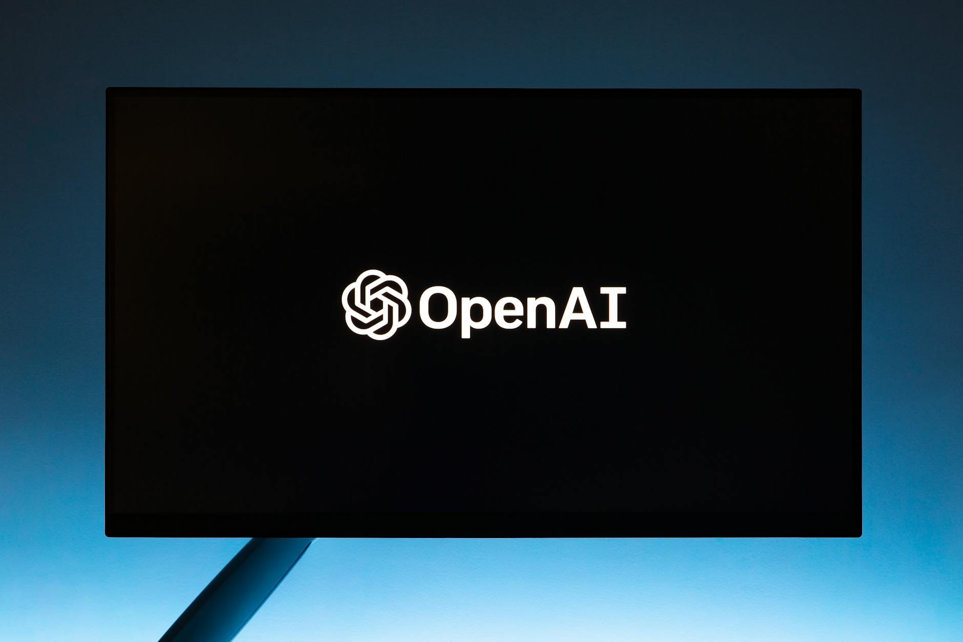 Logo OpenAI na ekranie na niebieskim, minimalistycznym tle gradientowym