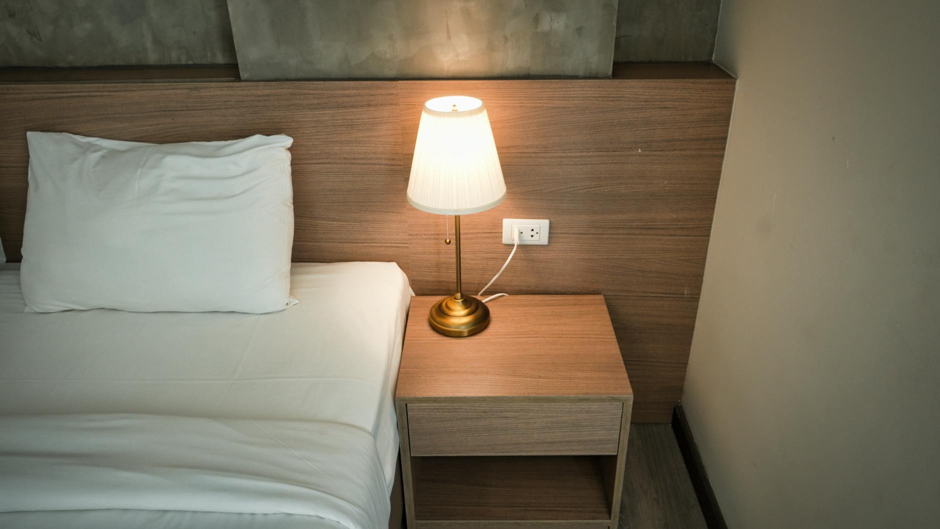 Instalacja elektryczna w sypialni jak zaplanować oświetlenie i gniazda przy łóżku Przytulna sypialnia z lampką na drewnianej szafce nocnej obok łóżka