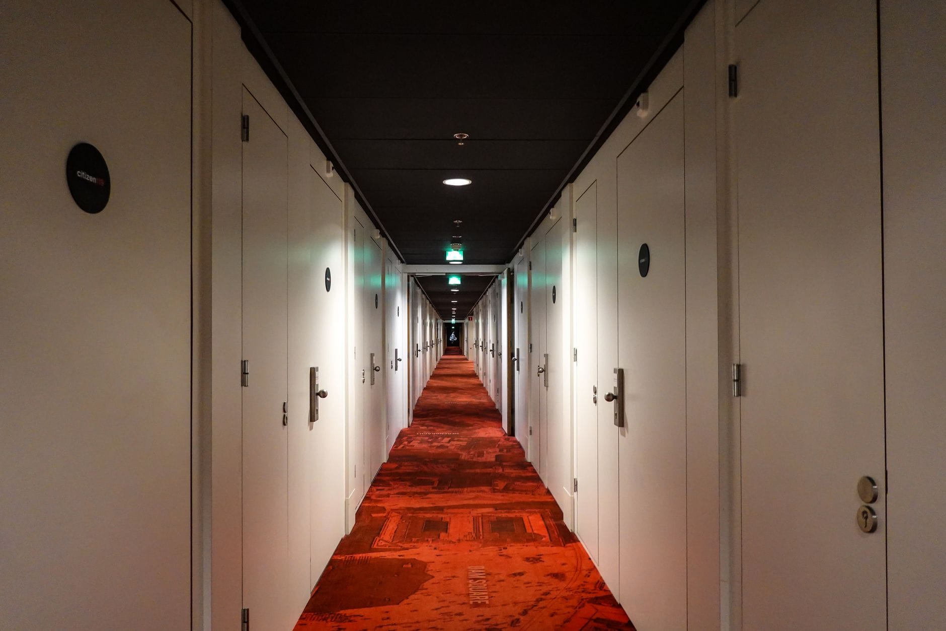 Jak urządzić funkcjonalny korytarz w domu szeregowym z wieloma drzwiami i małą ilością światła Długi hotelowy korytarz z czerwonym dywanem i licznymi białymi drzwiami