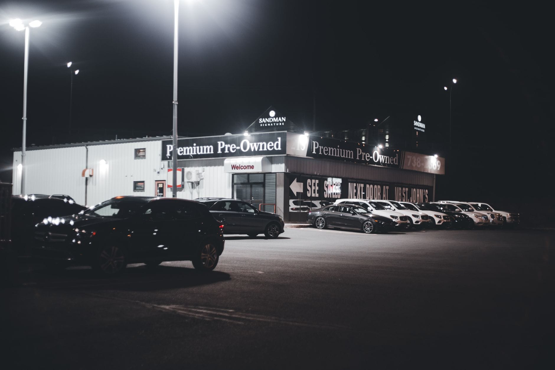 Jak bezpiecznie kupić używany samochód z Niemiec – poradnik krok po kroku dla początkujących kierowców Nocny plac salonu z podświetlonymi używanymi samochodami premium